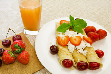 Dessert made from pancakes stuffed with curd cheese with strawberries and cherries is on a table in a white plate