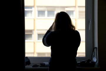 Fototapeta premium Back view of silhouette of a woman putting on makeup in front of a window