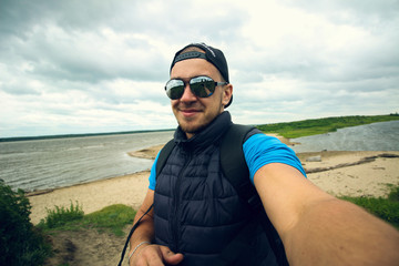 Man takes pictures of himself on the background of the river