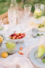 picnic, food, summer, holiday concept - close-up on wooden festive table with white tablecloth, dish with cherries, served with glass cups, goblets, glasses, fruit plates, pitcher of lemonade.