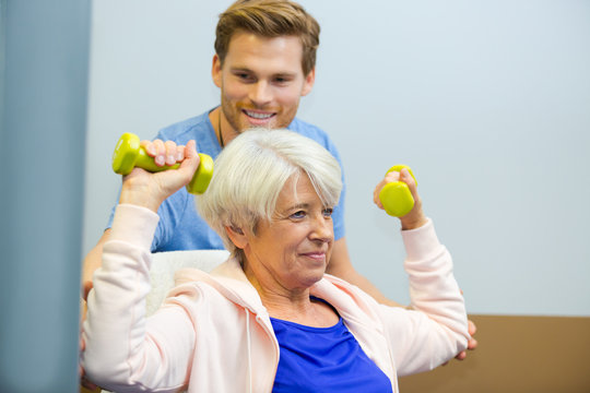 physiotherapist assisting senior woman to lift dumbbells