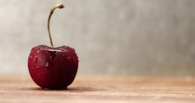 man's hand puts a cherry covered by drops on the table