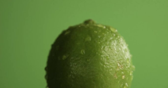lime turning on it's axis on green background covered by water drops