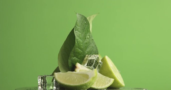 lime turning on it's axis on green background covered by water drops and with ice cubes