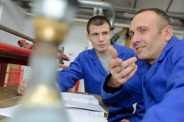 Fototapeta premium young technician working on machine in workshop with co-worker