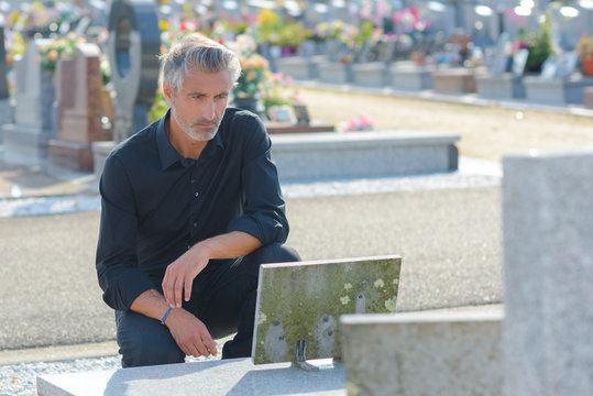 man placing flowers by headstone in cemetery