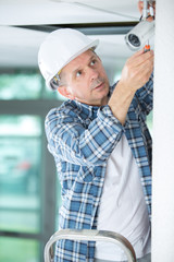 mature male technician installing camera on wall with screwdriver