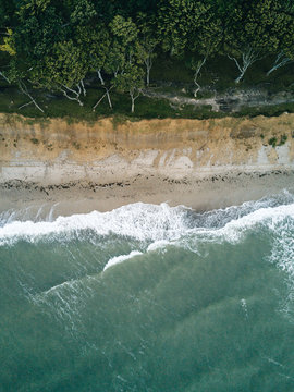 Aerial photo of coastline on a stormy day hitting a beach cliff overlooked by a forest