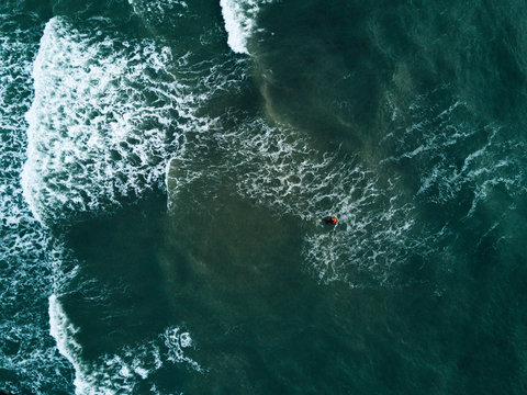 Aerial photo of a surfer swimming on waves on a stormy day