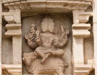 Nanjangud, India - October 26, 2013: Closeup of chiseled mural of multi-headed God Agni sitting on a bull in beige sandstone of the Mandapam at Srikanteshwara Temple.