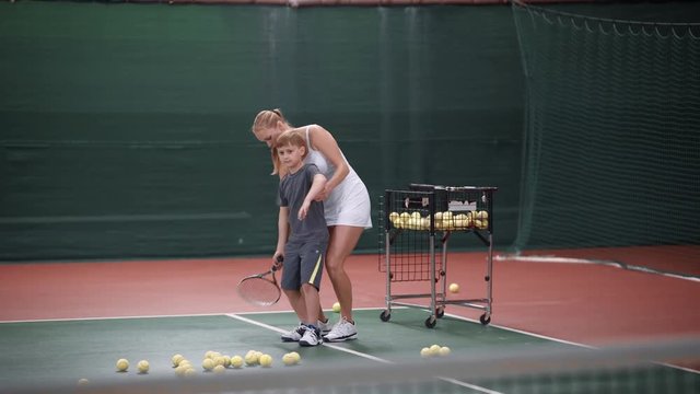 The little boy learns to play tennis, the guy and his teacher sort out the basics of tennis in a closed court, the teacher helps to beat the balls
