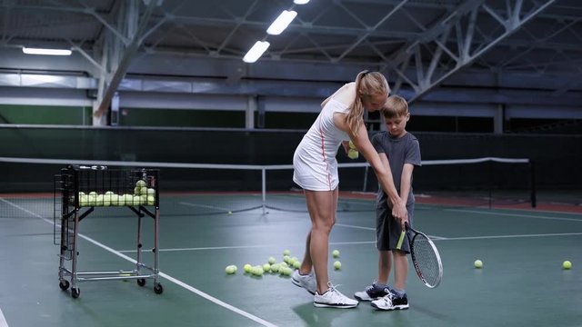 The young coach teaches an adult boy to keep the right racket, the student and his master are in a tennis club, people are dressed in tracksuits