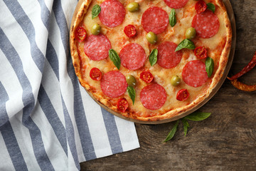 Pizza with salami on wooden table, top view