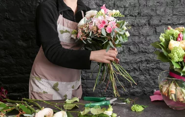 Papier Peint photo Lavable Fleuriste Female florist creating beautiful bouquet in flower shop on black brick wall background