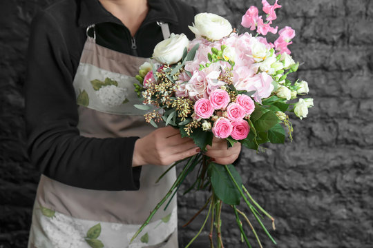 Female florist creating beautiful bouquet in flower shop on black brick wall background