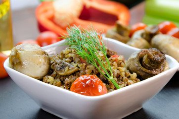 Dish from buckwheat with baked mushrooms, tomatoes, pepper. Decorated with a branch of fresh dill. In the background, a grease cup with olive oil, fresh red sweet pepper, celery. Home diet food.