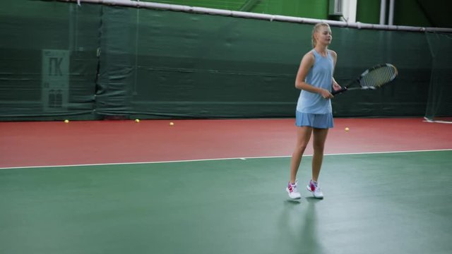 A teenager in a sports dress practices a tennis game in a sports club, the girl beats the balls through the net with a racket