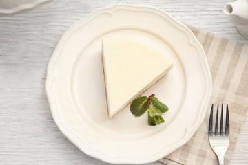 Plate with piece of delicious cheesecake on table