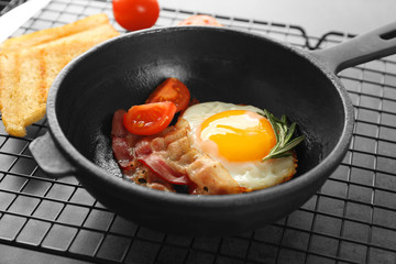 Frying pan with tasty egg and bacon for breakfast on table