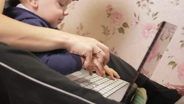 Young woman with her son sitting at home on the couch with a laptop. Look carefully at the screen and press the keys.