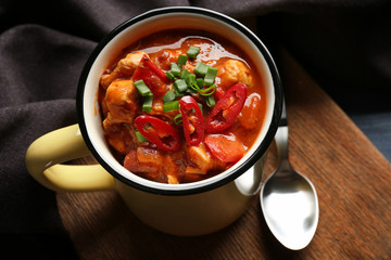 Enamel mug with delicious chili turkey on wooden board
