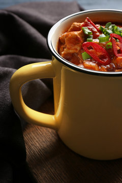 Enamel mug with delicious chili turkey on table, closeup