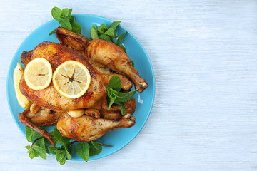 Plate with homemade baked chicken with lemon and mint on wooden background