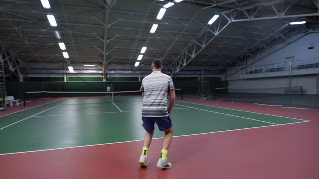 An adult man plays a match in tennis on a sports court, a person in a sporty form beats the ball with a racket in the gym