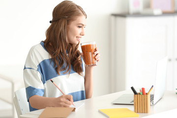 Weight loss concept. Beautiful young woman drinking healthy delicious smoothie and using laptop at home