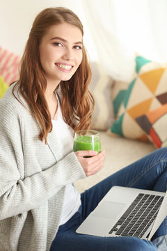 Weight loss concept. Beautiful young woman drinking healthy delicious smoothie and using laptop at home