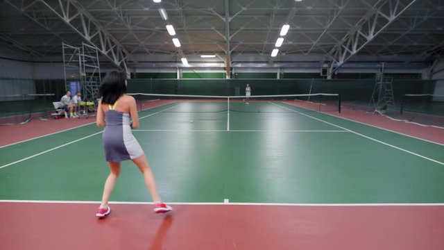A sports woman who is engaged in tennis beats the ball through the net, the tennis player plays with the opponent who wants to win the match
