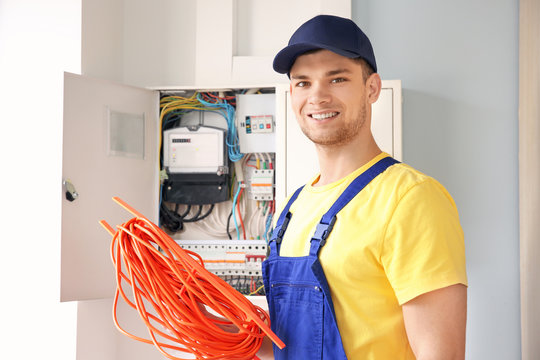 Young smiling electrician with bunch of wires standing near distribution board