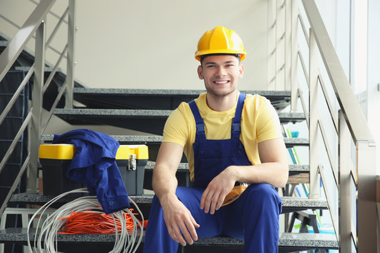 Young smiling electrician sitting on stairs indoors