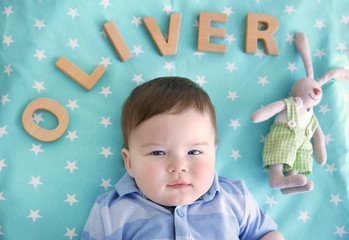 Cute baby lying on bed with word OLIVER composed of wooden letters. Choosing name concept