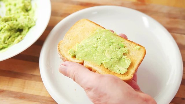 A man uses a fork to mash an avocado in a white dish