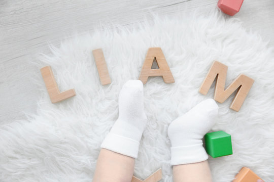 Legs of cute baby and word LIAM composed of wooden letters on floor. Choosing name concept