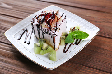Plate with tasty cake and chocolate sauce on wooden table, closeup