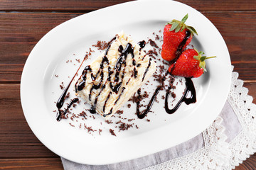 Plate with tasty cake, chocolate sauce and strawberries on wooden table