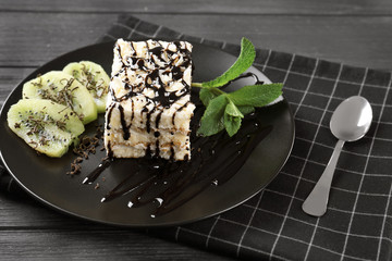 Plate with tasty cake and chocolate sauce on wooden table, closeup