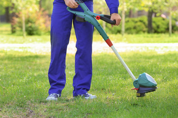 Young worker mowing lawn with grass trimmer outdoors on sunny day