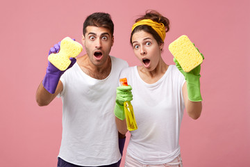 Portrait of funny emotional young Caucasian couple in rubber gloves having astonished and shocked...