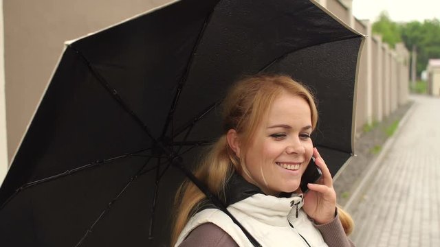Girl with long blond hair under an umbrella talking on the phone in a rainy day in the street.