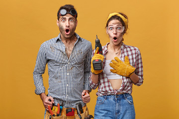 Beautiful female electrical technician with drill wearing protective gloves and goggles standing...