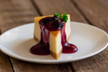 Homemade blueberry cheesecake on white plate decorated with parsley and blueberry sauce. Moist and smooth classic baked cheesecake. Copy space background of delicious blueberry New York cheesecake.