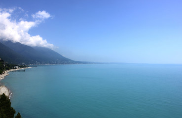 Summer landscape. Sea bay with town on coast at foot of mountains in clouds.