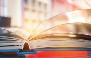 open book light on glass desk in color library room with blurred focus shelf background, education back school and learning concept