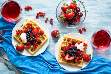 Healthy breakfast: Belgian waffles with sour cream, strawberry, raspberry, blueberry, cherry and red currant on blue wooden table. Selective focus