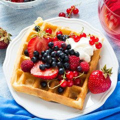 Healthy breakfast: Belgian waffles with sour cream, strawberry, raspberry, blueberry, cherry and red currant on blue wooden table. Selective focus