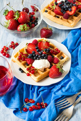 Healthy breakfast: Belgian waffles with sour cream, strawberry, raspberry, blueberry, cherry and red currant on blue wooden table. Selective focus