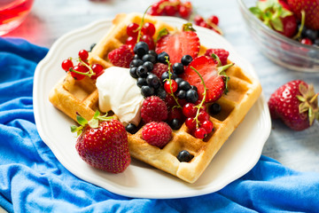 Healthy breakfast: Belgian waffles with sour cream, strawberry, raspberry, blueberry, cherry and red currant on blue wooden table. Selective focus